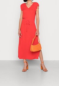 Robe rouge mi-longue avec manches à volants, taille cintrée, associée à un sac  à main orange texturé et des sandales à talons blocs orange.