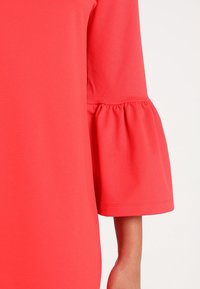 Rotes Kleid mit strukturierter Stoff, Glockenärmeln mit gerafften Akzenten und einem glatten Ausschnitt. Nahaufnahme der Ärmeldetails.