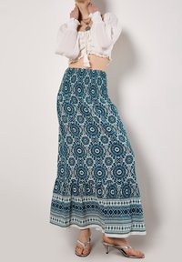 Blå och vit mönstrad maxikjol med elastisk midja. Har blommönster och en texturerad fåll. Bärs med en vit kort topp.