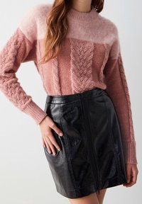 Pink and cream cable knit sweater with long sleeves, paired with a black glossy leather mini skirt featuring a front zipper.