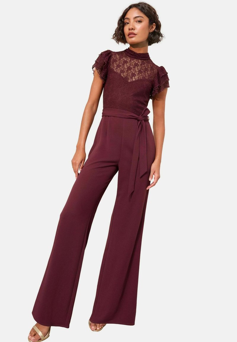 Mono burdeos con mangas cortas de encaje, corsé ajustado y pantalones de pierna ancha. Presenta una cintura ceñida con cinturón y un top texturizado. Tela suave.