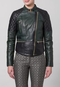Zelená kožená bunda s černými prošívanými rameny, obsahující zlaté zipy, úzký střih a texturovanou černou koženou dolní část.