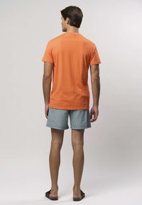 Oranžové bavlnené tričko v kombinácii s modrobielo pruhovanými krátkymi nohavicami, doplnené hnedými šľapkami; pohľad zozadu zobrazuje jednoduchý dizajn.