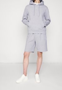 Sudadera gris con bolsillo frontal y cordones, combinada con pantalones cortos grises a juego. Zapatillas blancas completan el look casual y cómodo.