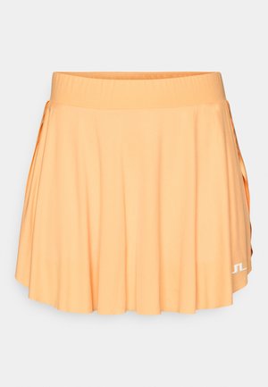 Plissert tennis skjørt i myk oransje stoff, med en bred elastisk midje og en hvit logo aksent på nedre høyre side.