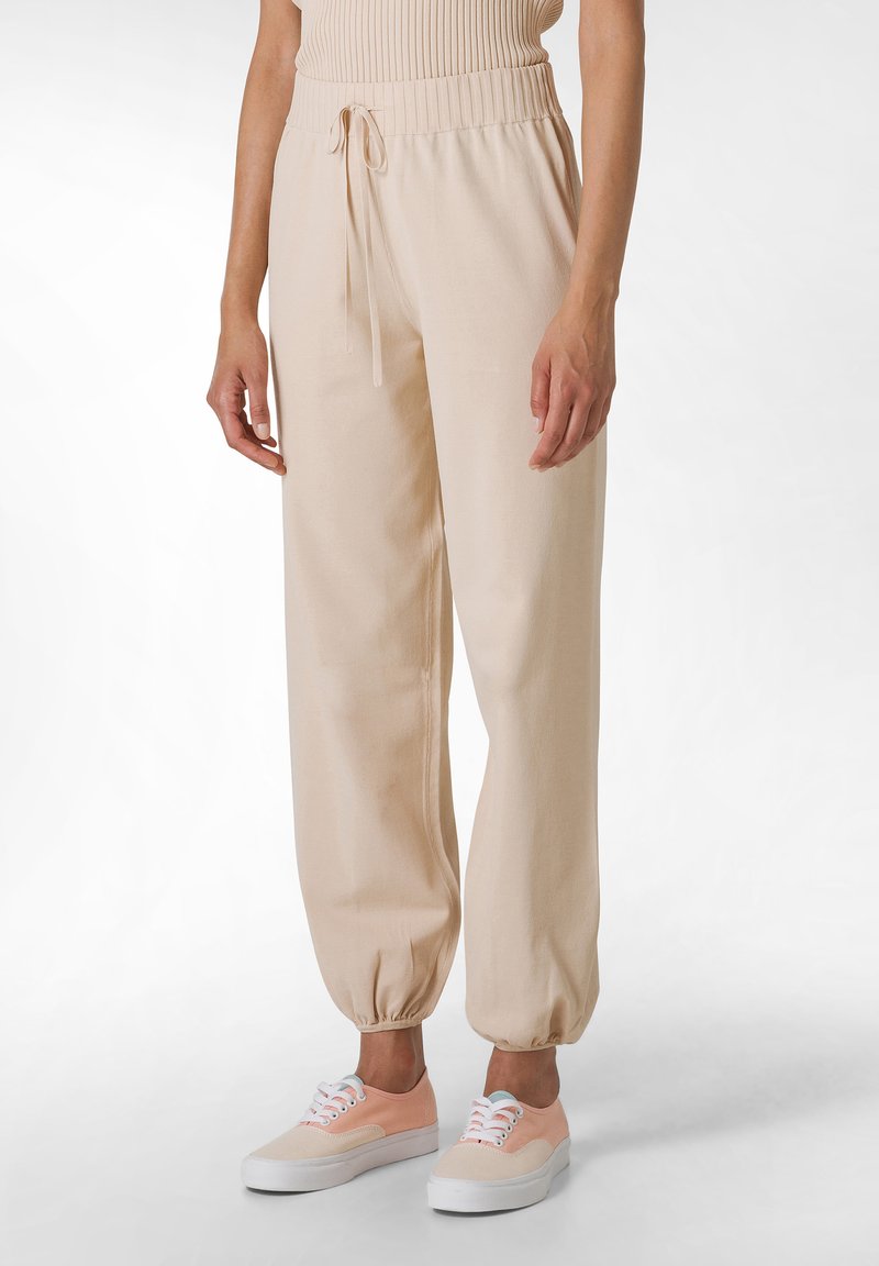 Beige jogger pants with an elastic waistband and drawstring. Fabric appears soft with gathered cuffs. Paired with pastel sneakers.