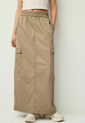Khaki Maxirock mit elastischem Bund, Seitentaschen, leichtem Material und schlankem Design, kombiniert mit beigen Sneakers.