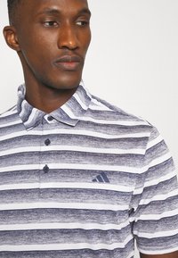 Prúžkovaná polo košeľa v námorníckej modrej a bielej farbe, s golierom, tromi gombíkmi a logom Adidas v námorníckej modrej na ľavej hrudi. Textúrovaná tkanina.