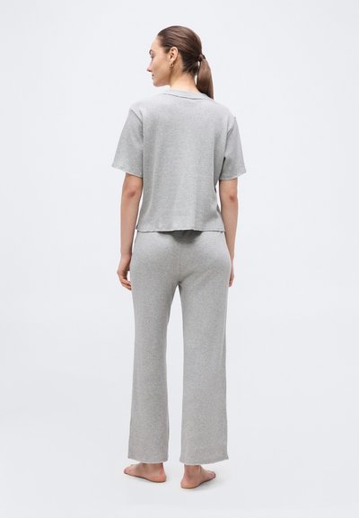 Γυναίκα με τα μαλλιά της δεμένα πίσω, όρθια και ξυπόλυτη, φοράει ένα ασορτί ανοιχτό γκρι χαλαρό τοπ με κοντά μανίκια και παντελόνια φαρδιάς γραμμής, κοιτώντας προς τα πίσω.