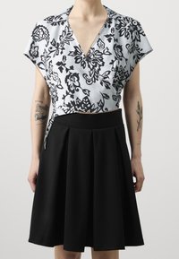 Blusa a maniche corte con motivo floreale in blu chiaro e nero, abbinata a una gonna nera plissettata. Tessuto morbido, design a scollo a V.