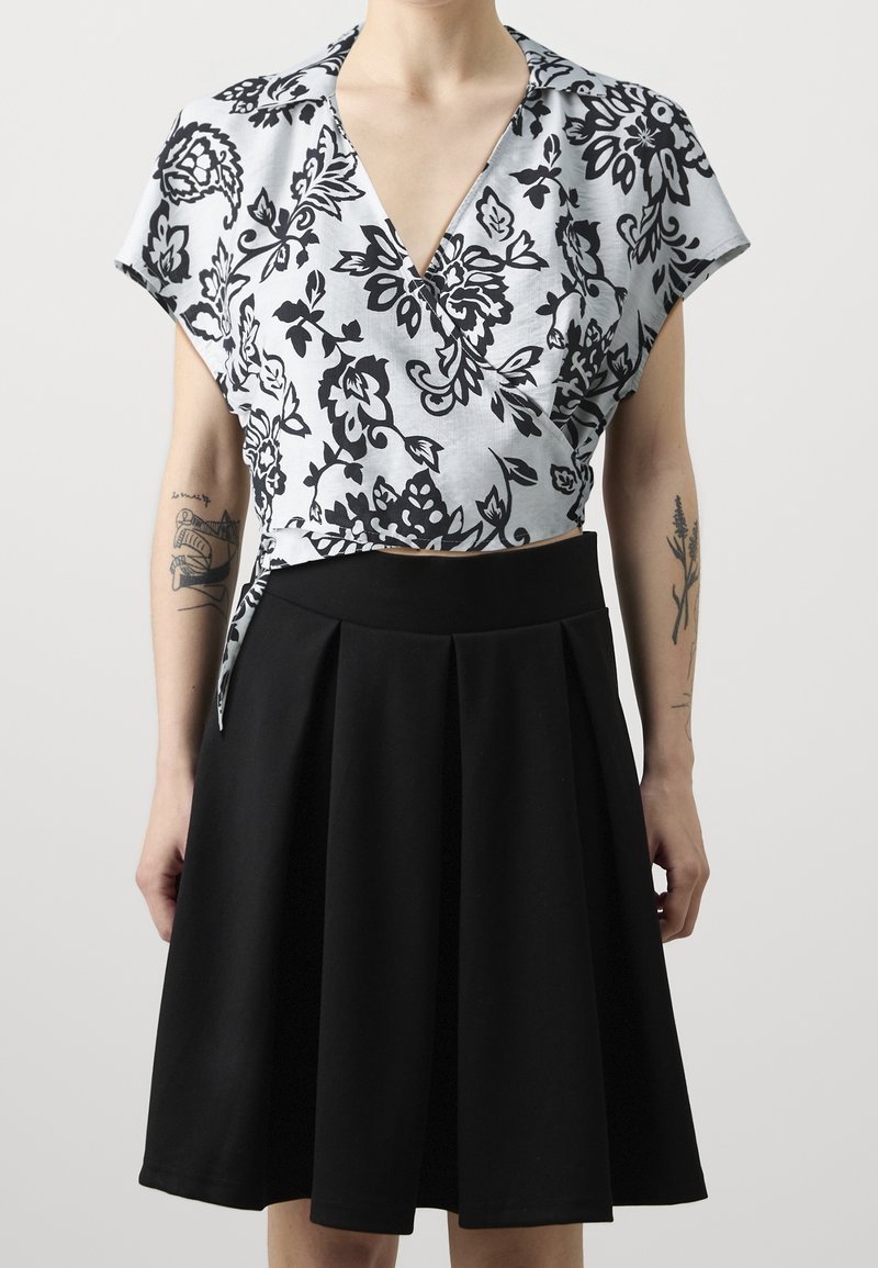 Blusa a maniche corte con motivo floreale in blu chiaro e nero, abbinata a una gonna nera plissettata. Tessuto morbido, design a scollo a V.