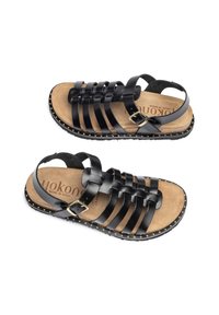 Sandalias de cuero negro con tiras y hebillas en el tobillo, plantillas acolchadas de color tostado y pequeños remaches dorados alrededor de los bordes de la suela negra.