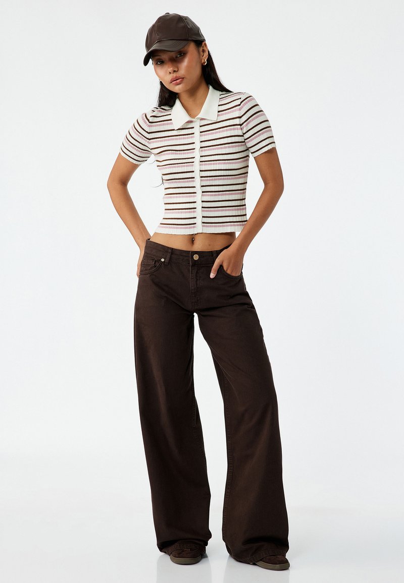 Stribet cropped top med krave i creme og brun. Sættes sammen med højttaljede, vide brune bukser. Model iført en brun kasket.