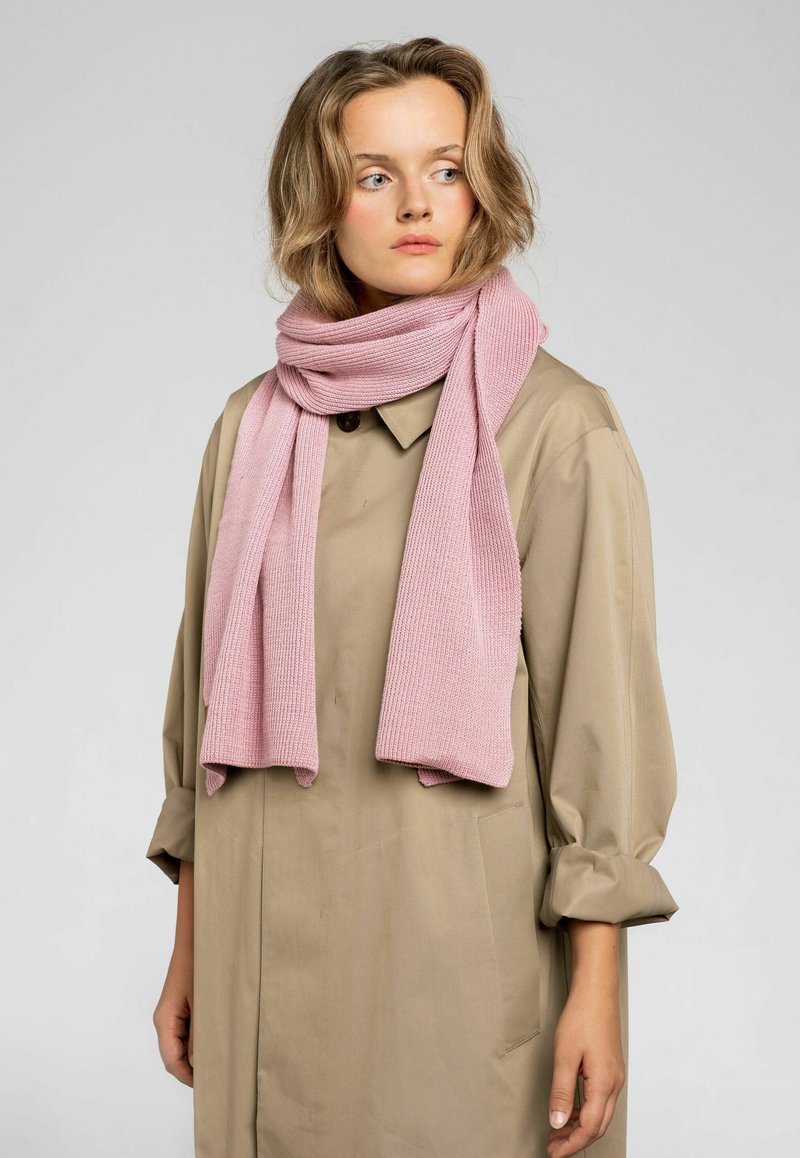 Różowy dzianinowy szalik o teksturowanym prążkowanym wzorze, zarzucony na szyję, w połączeniu z beżowym płaszczem z kołnierzykiem i mankietami.