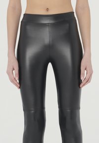 Zwarte faux leren leggings met een gladde, glanzende textuur, hoge tailleband en naaddetails bij de knieën, ontworpen voor een aansluitende silhouet.