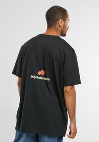 Tricou din bumbac negru, cu o croială lejeră, având un grafic cu zaruri roșii și textul "lady luck casino" în galben pe spate. Guler rotund și mâneci scurte.