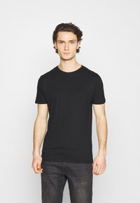 Camiseta de algodón negra con mangas cortas y cuello redondo, exhibida en un entorno neutral. Presenta una textura suave y un diseño simple.