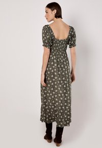 Robe midi vert olive avec imprimé floral blanc, corsage smocké, manches courtes bouffantes et dos carré. Fabriquée en tissu léger.