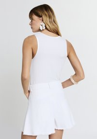 Un débardeur blanc à côtes associé à un short en denim blanc avec un ourlet effiloché. Accessoirisé avec de grandes boucles d'oreilles florales et un bracelet.