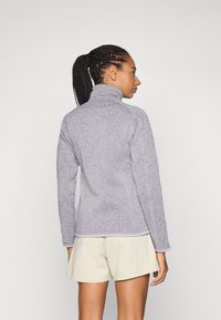 Grijze fleece pullover met een hoge kraag en lange mouwen, voorzien van een subtiele gespikkelde textuur en contrasterende lichte afwerking aan de onderrand.
