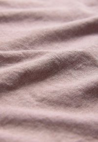 Šviesiai rožinė medvilnės medžiaga su minkšta tekstūra, rodanti subtilius raukšles ir nuosekliai austą raštą per visą paviršių.