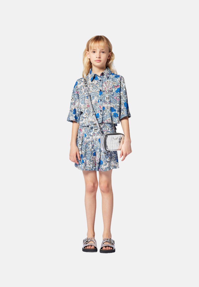 Chemise à manches courtes avec un motif floral bleu et un short assorti au design cropped. Associé à un sac bandoulière en argent et des sandales noires.