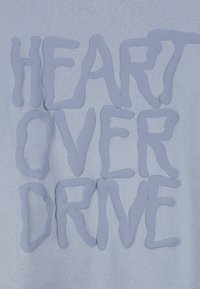 Lichtblauwe stof met een verhoogd tekstontwerp waarop "HEART OVER DRIVE" staat, in een afgerond, onregelmatig lettertype. Zachte textuur met een matte afwerking.