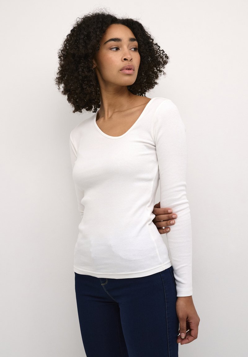 Witte longsleeve top in een geribde textuur met een ronde hals, gecombineerd met donkerblauwe jeans. Eenvoudig ontwerp, aangesloten silhouet.