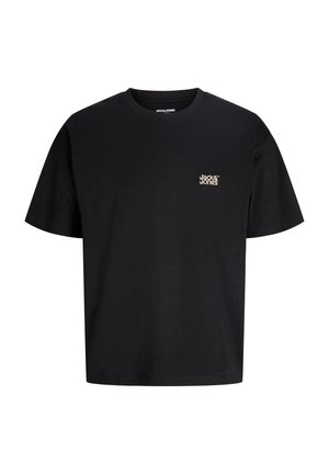 Garçon portant un t-shirt noir Jack & Jones et un pantalon camouflage, debout, mains le long du corps, souriant et regardant vers la gauche.