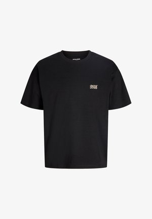 Dreng iført en sort Jack & Jones T-shirt og camouflagebukser står med hænderne ned langs siden, smilende og kigger mod venstre.