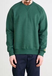Groen sweatshirt gemaakt van zachte stof, met een ronde hals, lange mouwen en geribde manchetten met een logopatch op de linker mouw.