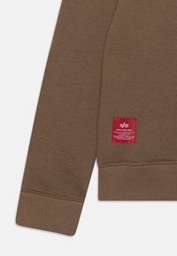 Brun sweatshirt med ribbade muddar och nederkant. Inkluderar en röd etikett sydd på undersidan som visar varumärket och tvättråd.