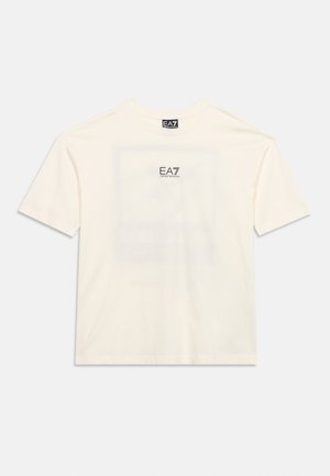 Valge lühikeste varrukatega T-särk, millel on EA7 Emporio Armani logo rindkere keskel ja kaelal silt, pildi taust on ühtlane.