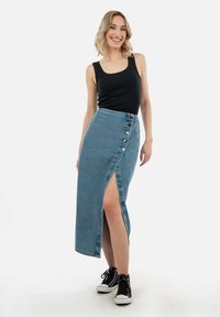 Denim maxi rok met een diagonale voorknof, voorzien van vijf knopen aan de zijkant, gecombineerd met een strakke zwarte tanktop en zwarte sneakers.
