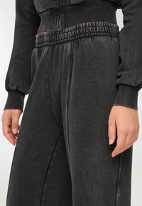 Zbliżenie na osobę w czarnych, wyblakłych spodniach dresowych z elastycznym paskiem i ściągaczami na rękawach pasującej bluzy.