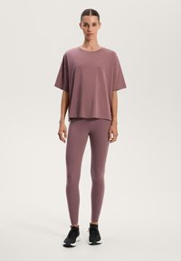 Lys lilla atletisk top med kort ærmer, parret med matchende leggings og sorte sneakers, der viser et tætsiddende design og glat tekstur.