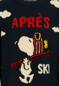 Ciemnoniebieski sweter z dzianiny z postacią Snoopy, z czerwonymi akcentami i napisem "APRÈS SKI" oraz białymi chmurkami. Grafika jest wyraźnie widoczna.