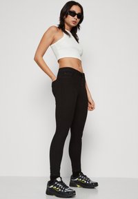 Jeans negros ajustados con cintura alta, combinados con un top corto blanco. Llevado con zapatillas negras que tienen detalles en gris y amarillo.