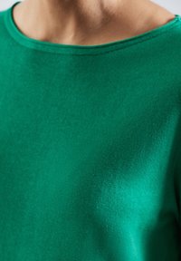 T-shirt vert à manches courtes avec un large col, une texture lisse et un tissu doux et léger. Peu de coutures et des lignes épurées sont visibles.