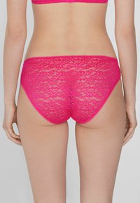 Spitzenunterwäsche in leuchtendem Pink mit floralem Muster. Sie zeichnet sich durch eine weiche Textur und gewellte Kanten aus und ist für einen bequemen Sitz konzipiert.