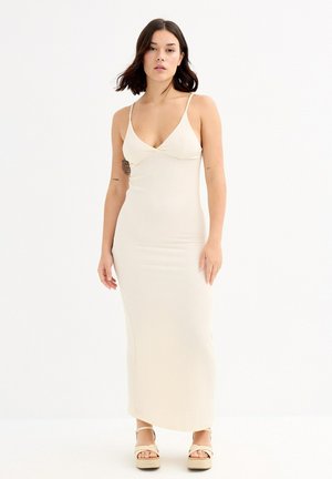Vestido maxi ceñido de crema con tirantes ajustables, escote en V y suave textura de canalé. Combinado con sandalias de plataforma beige.
