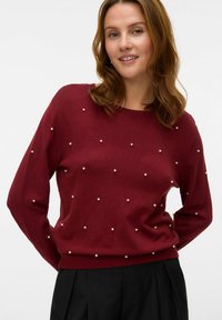 Burgundowa dzianinowa sweter z okrągłym dekoltem, zdobiony małymi per�łowymi elementami równomiernie rozmieszczonymi na przodzie, luźny krój, długie rękawy.