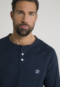 Marineblauwe langemouwen henley-shirt van katoen. Beschikt over een ronde hals, drieknoopsluiting en geborduurd logo op de linkerborst.