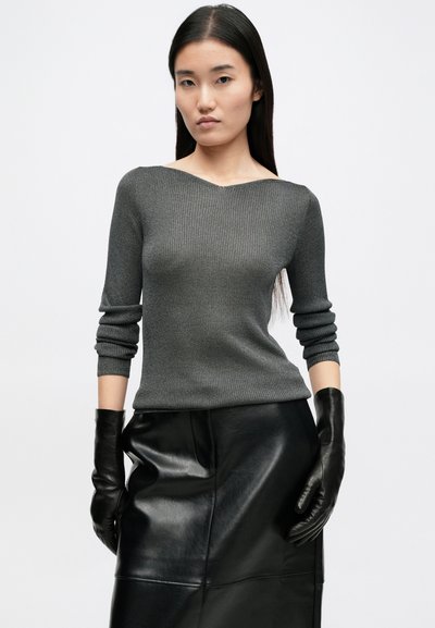 Γκρίζος ριμπές πουλόβερ με V λαιμόκοψη και μακριά μανίκια, συνδυασμένο με μαύρη δερμάτινη φούστα και μαύρα γάντια, δημιουργώντας ένα πολυεπίπεδο στυλ.