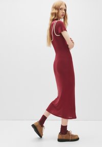 Bordo obleka s kratkimi rokavi in belimi detajli. V kombinaciji s svetlo rjavimi čipkastimi čevlji in bordo nogavicami, ki poudarjajo eleganten silhuet.