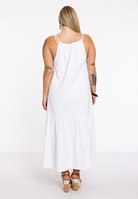 Weißes, gestuftes Maxikleid mit verstellbaren Spaghettiträgern und gerafftem Rücken. Verfügt über einen fließenden Stoff und einen lockeren Schnitt.