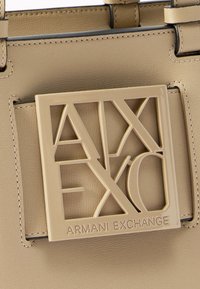 Τσάντα από μπεζ δέρμα με μεγάλη, τετράγωνη πλακέτα με το λογότυπο Armani Exchange στο ίδιο μπεζ χρώμα στο μπροστινό μέρος.