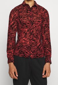 Camicia a righe zebrate rossa e nera con maniche lunghe, chiusura con bottoni e design aderente. Tessuto morbido con una leggera lucentezza.