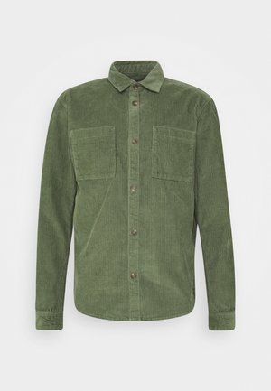 Camisa de botones de pana verde con collar, dos bolsillos en el pecho y cierre de botones. Presenta una tela texturizada y mangas largas.