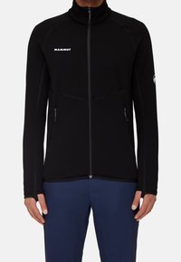 Giacca in pile nera con colletto alto, zip completa e tasche con zip. Presenta cuciture a contrasto e un logo sul petto.
